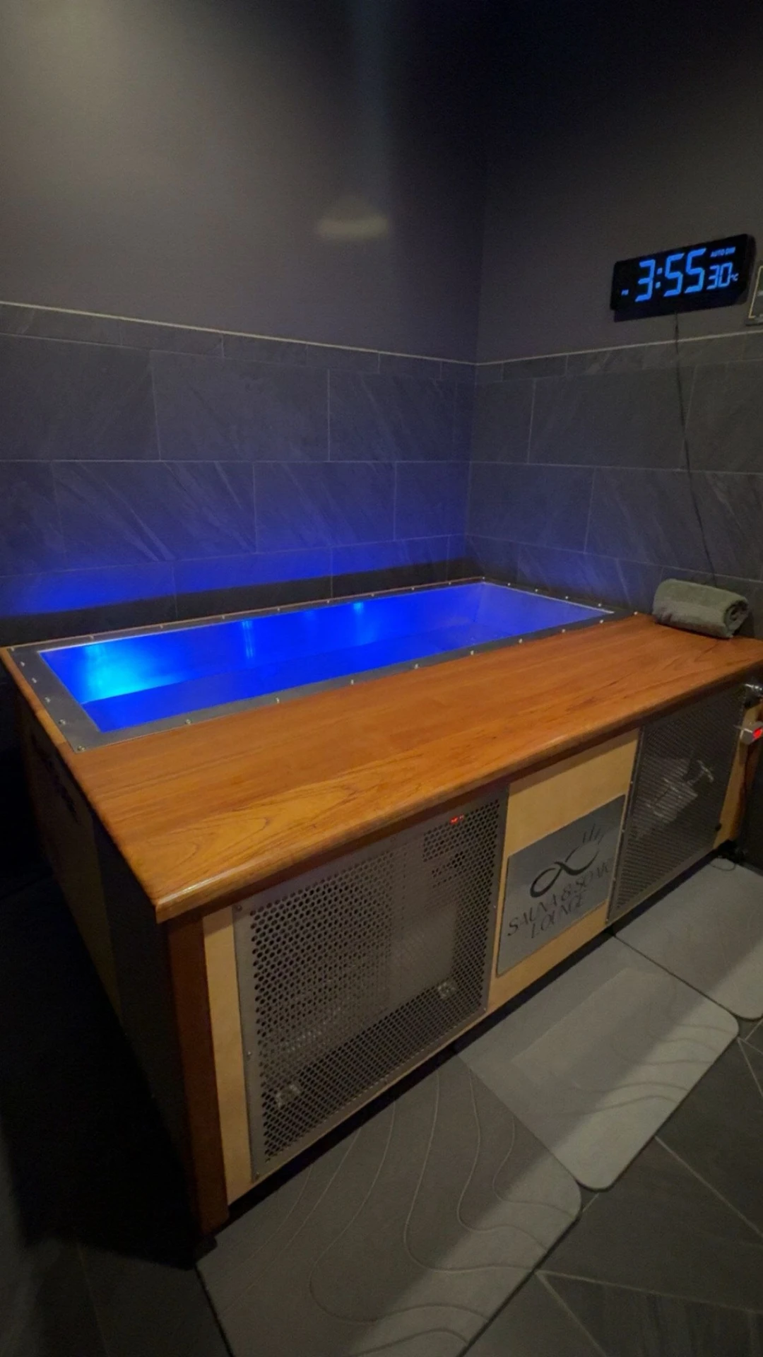 BlueCube cold plunge with timber surround, glowing blue water, rolled towel, and digital timer