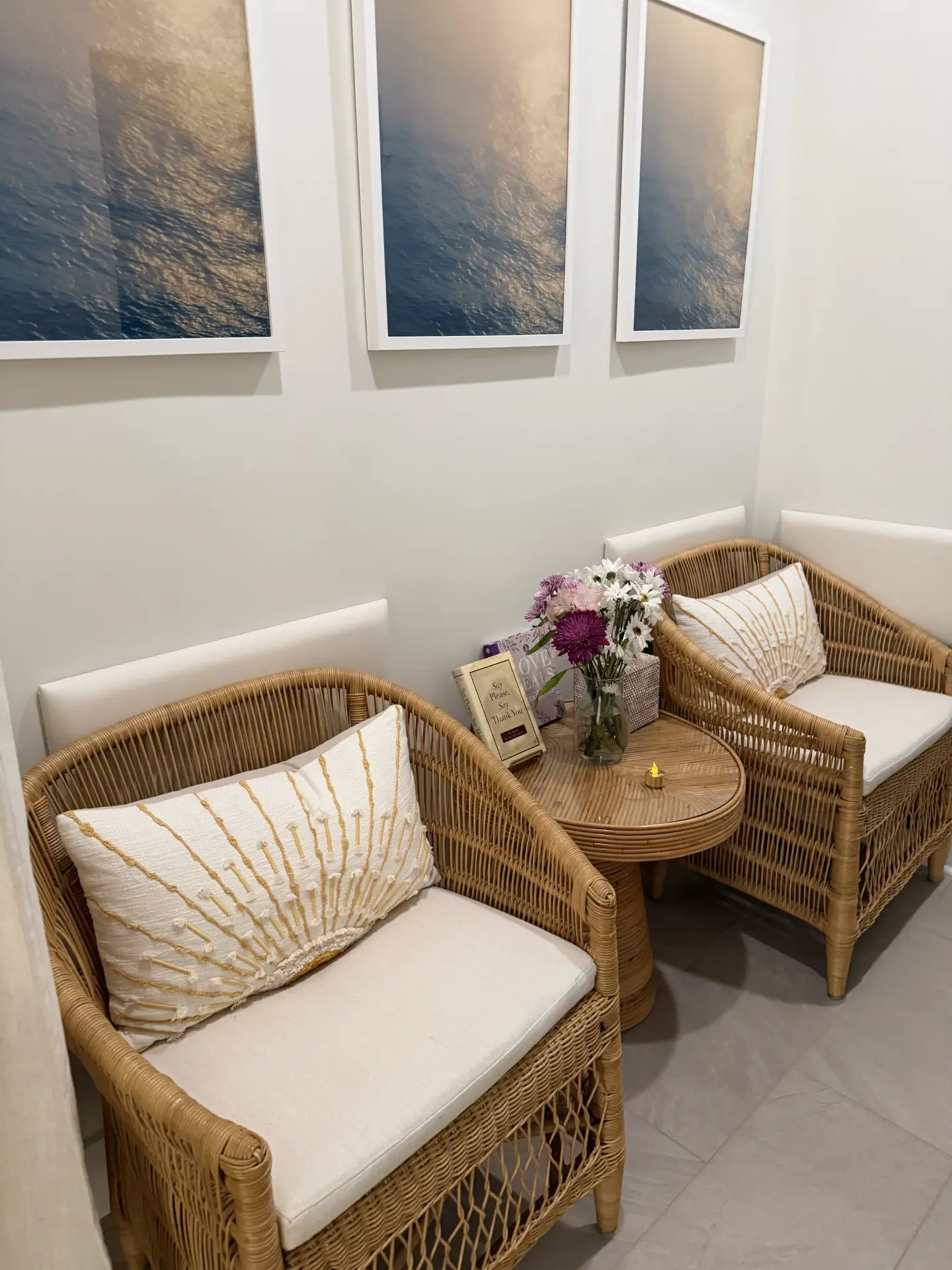 Wicker lounge chairs with cream cushions, ocean artwork, and fresh flowers in the waiting area