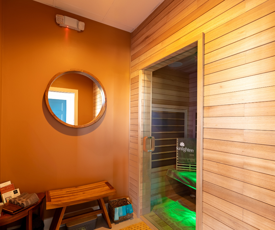 Sunlighten infrared sauna suite with warm cedar walls, round mirror, and green chromotherapy lighting