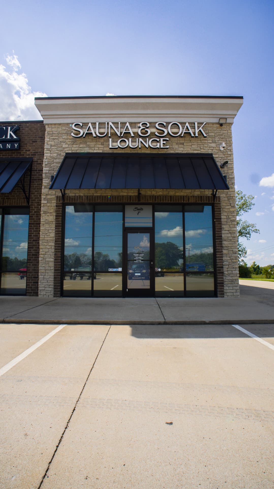 Exterior of the Sauna & Soak Lounge storefront with stone facade, black awning and illuminated sign