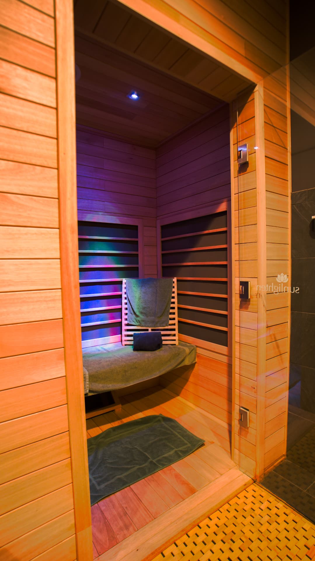 Private cedar infrared sauna suite lit with purple and blue chromotherapy, towels folded on the bench